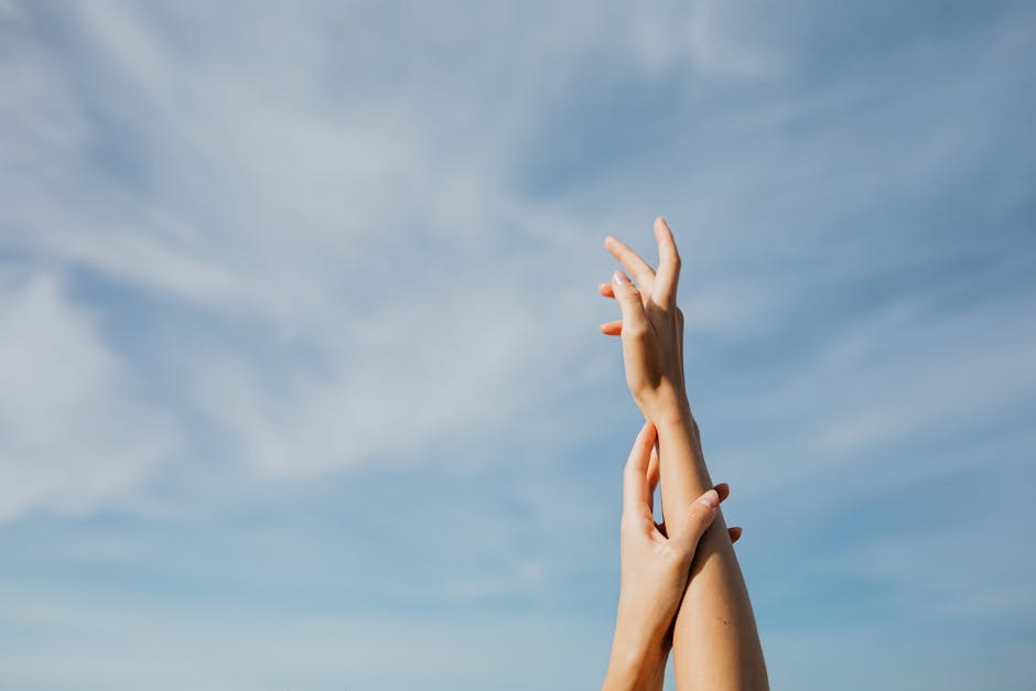 Two adult hands reaching up in front of a clear blue sky, symbolizing freedom and aspiration.